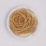 Yellow gold Bubble Bracelets in various sizes coiled in a white marble bowl, against a white background.