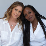 Two women each wearing Enamel Gold Unity Pendants - Large with a white shirt against a light grey background. 