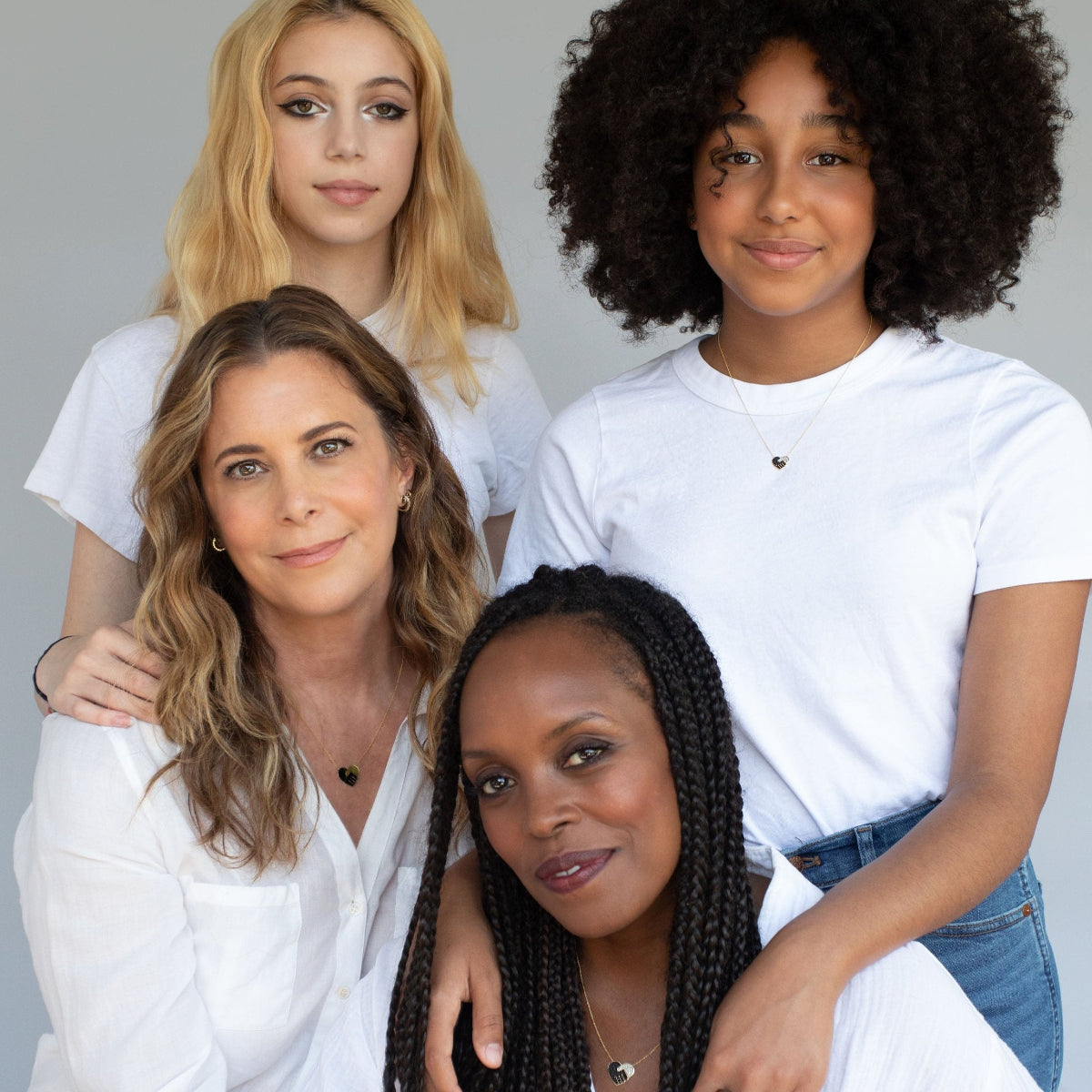Two women and their daughters all wearing the Enamel Gold Unity Pendant, styled with white tops against a light grey background.