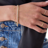 A close-up of a hand wearing a yellow gold  Custom Gold Bracelet - 3 letters (Z, O, E), a Love Set Match Bracelet and an Element Long Link Bracelet, a Pavé Diamond Ring and a Link Ring. 