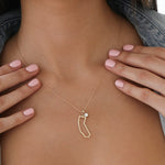 Close-up of a woman's decellotage wearing a California Necklace with a Duchess Diamond Pendant, held by her hands with light pink nails. 