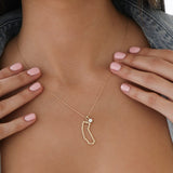 Close-up of a woman's decellotage wearing a California Necklace with a Duchess Diamond Pendant, held by her hands with light pink nails. 