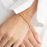 A close-up of hands wearing a yellow gold Rolo Bracelet and an Element Long Link Bracelet, with a white shirt. 