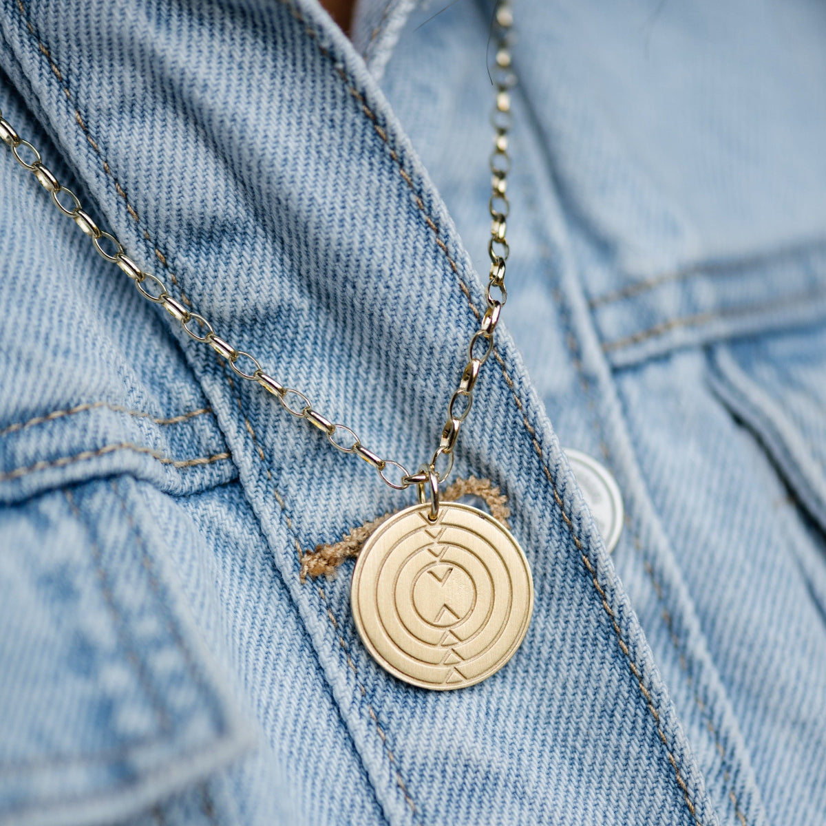 Close-up of a Virtues Pendant - Circle in yellow gold on top of a blue denim jacket. 