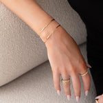 A hand wearing two Off the Cuff Bracelets, an Etched Paris Ring and The Evermore Ring, all in yellow gold, against a neutral background. 