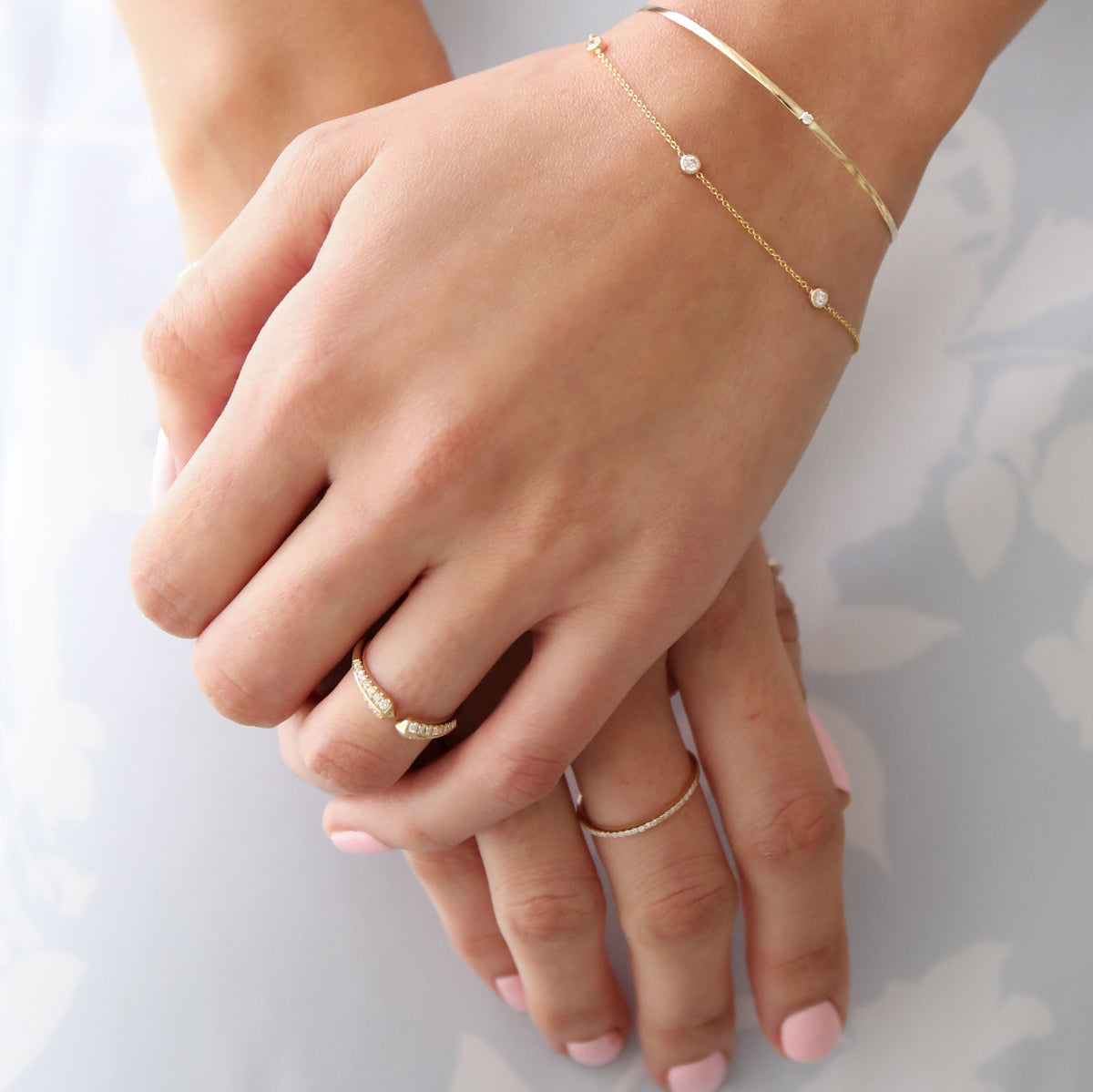 A close-up of a woman’s hands wearing an Off the Cuff Bracelet, a Starstruck Diamond Bracelet, an Open Diamond Ring and a Pavé Diamond Ring, against a white and light grey background.