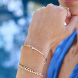 A close-up of a woman’s hand wearing a Doubles Cuff, a Love Set Match Bracelet, an Off the Cuff Bracelet and a Geo Stacking Ring, styled in a blue top.