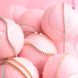 Several bracelets in yellow and white gold, including two Tie Breaker Bracelets, two Bubble Bracelets, two Down the Line Bracelets and a Doubles Cuff, laid on several light pink tennis balls.