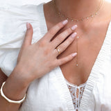 Close-up of a woman’s décolletage and hand wearing a Diamond Drip Necklace, a Stardust Diamond Necklace, a Tenfold Hinge Bracelet and a Tenfold Ring, styled in a white top.