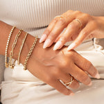 A close-up of a woman’s hands wearing a Love Set Match Bracelet, a Down the Line Bracelet, an Element Long Link Bracelet, an Element Short Link Bracelet and a Rolo Bracelet, as well as a Criss-Cross Duo Ring, a Criss-Cross Diamond Duo Ring and a Criss-Cross Diamond Daze Ring, all in yellow gold, styled in neutral clothing.