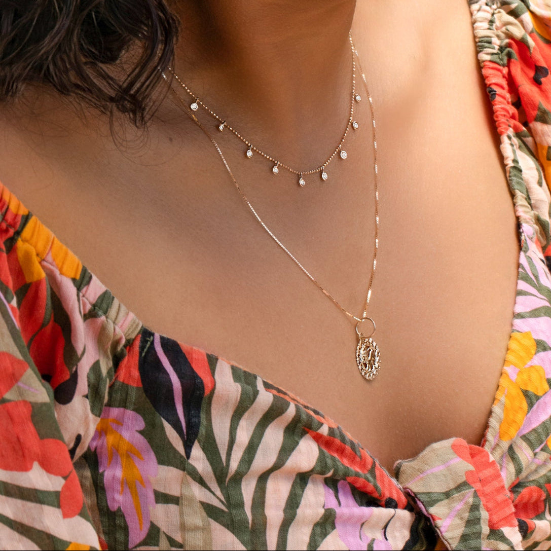 A woman's décolletage wearing a Stardust Diamond Necklace and a Zodiac Necklace, with a colorful floral top. 