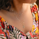 A woman's décolletage wearing a Stardust Diamond Necklace and a Zodiac Necklace, with a colorful floral top. 