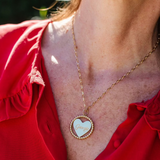 Close-up of a person's neck wearing a yellow gold Be Gentle in Grief Necklace engraved with 'Georgie,' paired with a red shirt and a blurred background.