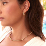 Close-up of a woman wearing a Link Hoop and a Rolo Bracelet in yellow gold, with brown hair and a white top against a blurred background.