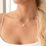 Close-up of a woman's décolletage wearing a C'est Moi Deco Necklace in yellow gold, with a white singlet top.