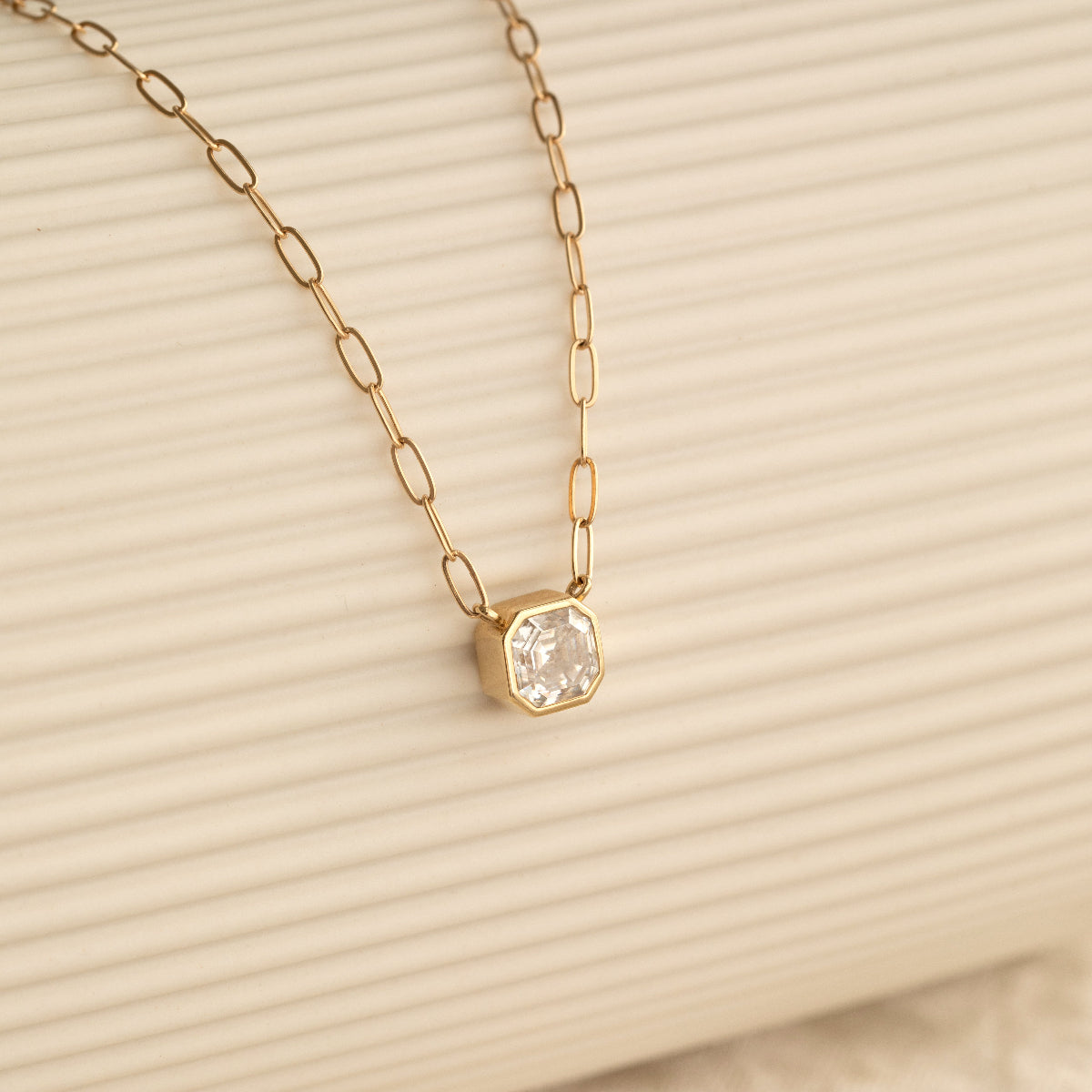 A C'est Moi Deco Necklace in yellow gold against a cream stripe background. 