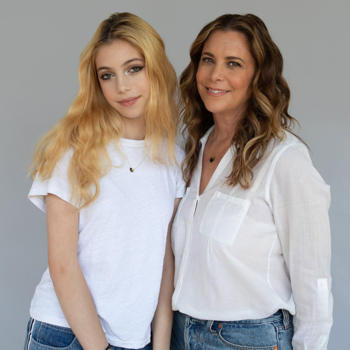 Maya Brenner and her daughter each wearing an Enamel Gold Unity Pendant (one small and the other large) with a white top and blue jeans against a light grey background. 