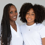 A mother and daughter each wearing a Pavé Unity Pendant (one large and one small), styled with white tops against a light grey background. 