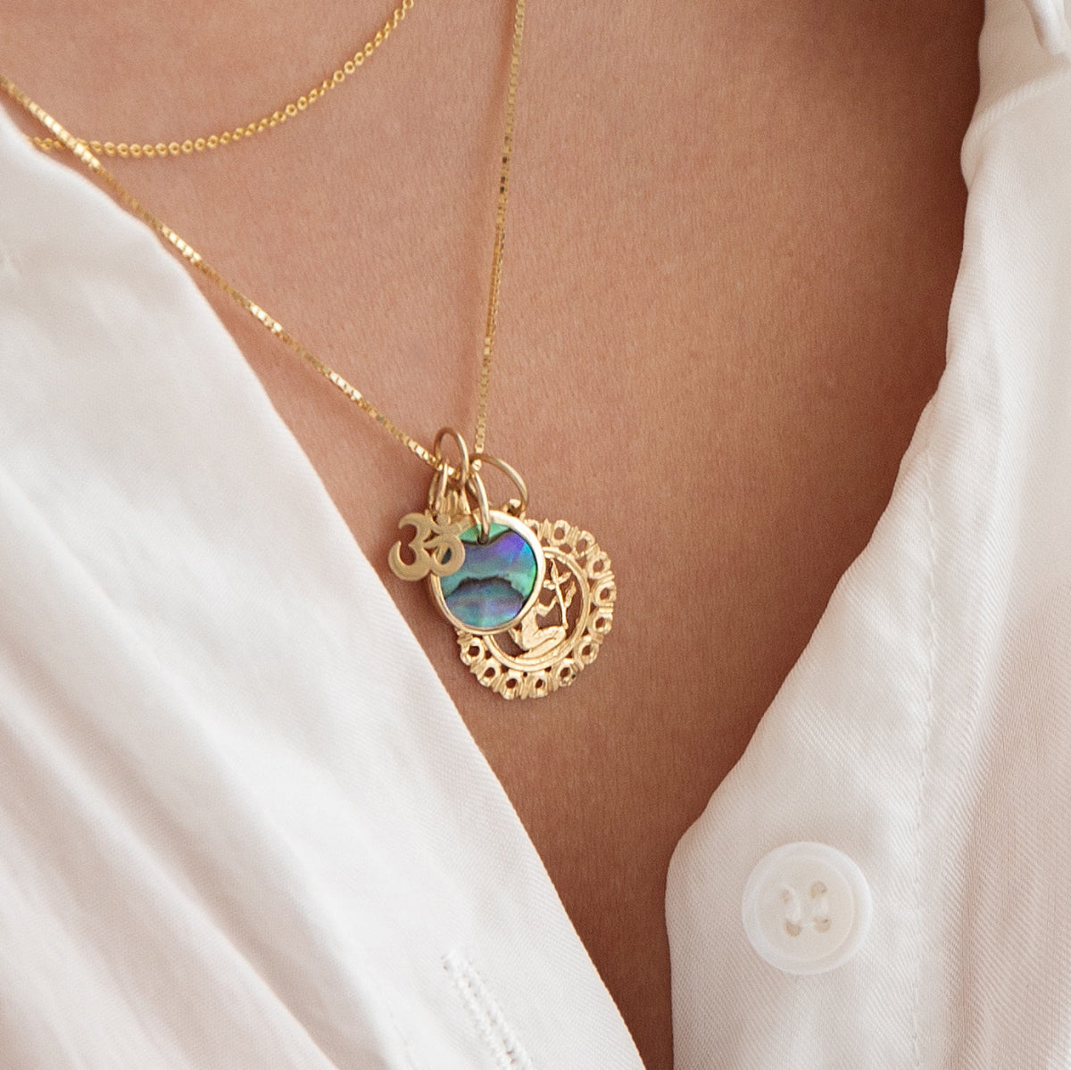 Close-up of a décolletage wearing a Zodiac Necklace - Virgo with a Small Abalone Cabochon Charm and an Om Charm Pendant, with a white shirt.