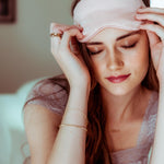 A woman wearing a yellow gold Diamond Cut Bracelet and rings, in a pink sleep mask with a soft, blurred background.