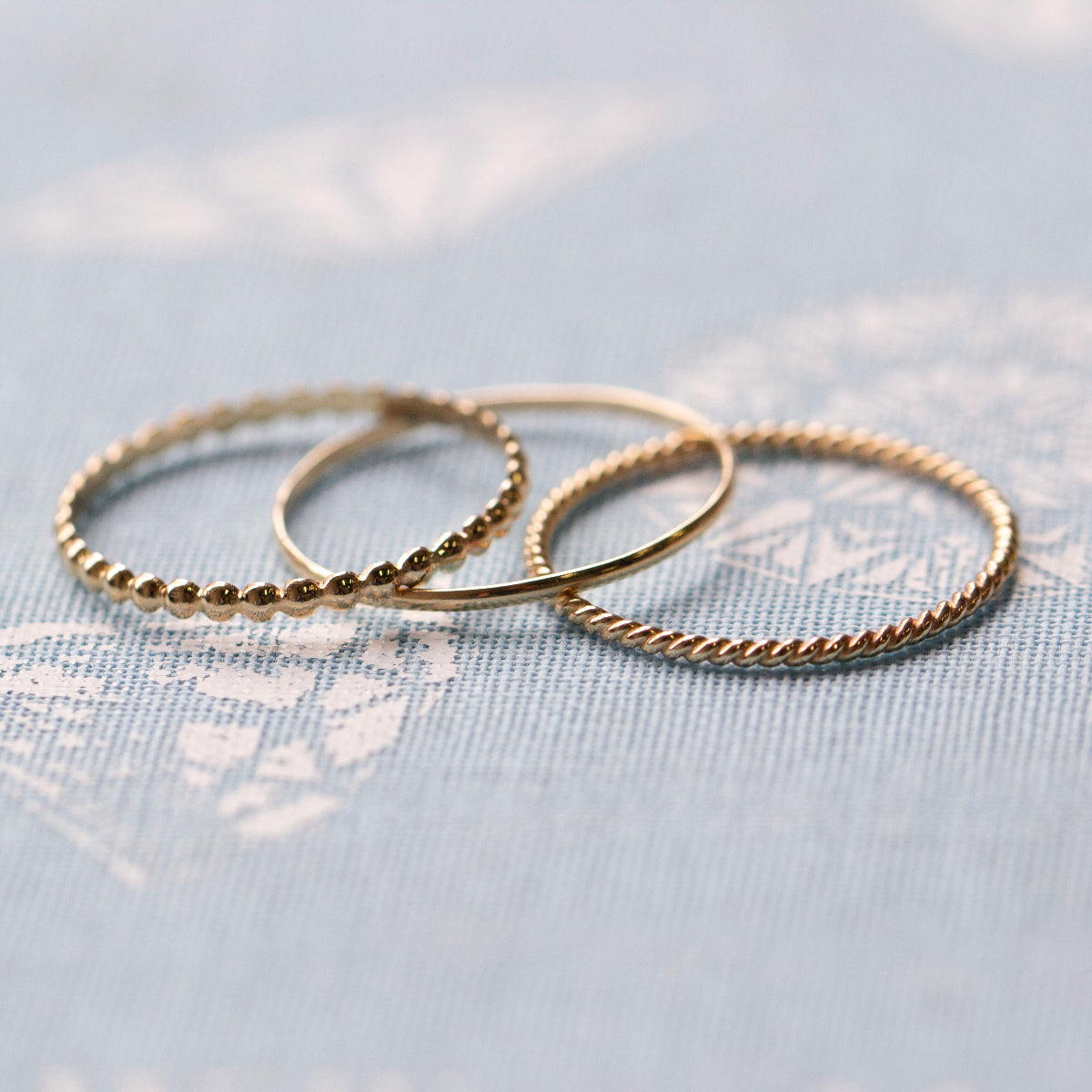 Delicate Trio Stacking Rings on a light blue textured background. 