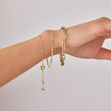 An arm wearing The Slide Heart Bracelet, Overboard Bracelet and Bold Link Bracelet, all in yellow gold against a light grey background.