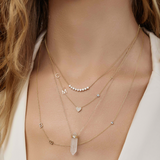 A close-up of a woman’s neck wearing four yellow gold necklaces: two Custom Gold Necklaces (one with three charms and the other with four charms), the Clarity Retreat Necklace and the Diamond Arc Layering Necklace, with a cream top.