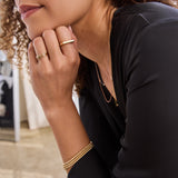 Close-up of a woman wearing a yellow gold Geo Stacking Ring | Square, Delicate Band, Pave Diamond Ring, two 4 Diamond Rings and three Classic Bubble Bracelets with a black top, against a softly blurred background.  
