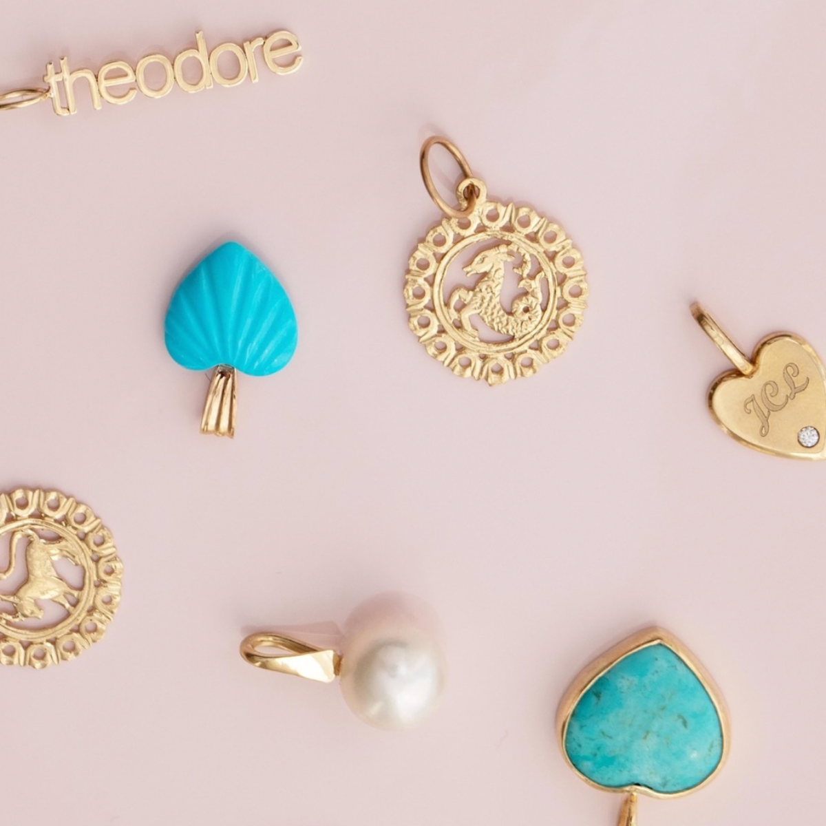 Several yellow gold and turquoise pendants and charms, including Zodiac Pendants, Petite Nameplate Pendants, a Perla Pendant, a Turquoise Heart Charm, an Etched Turquoise Heart Charm and an Engraved Heart Charm on a light pink background. 
