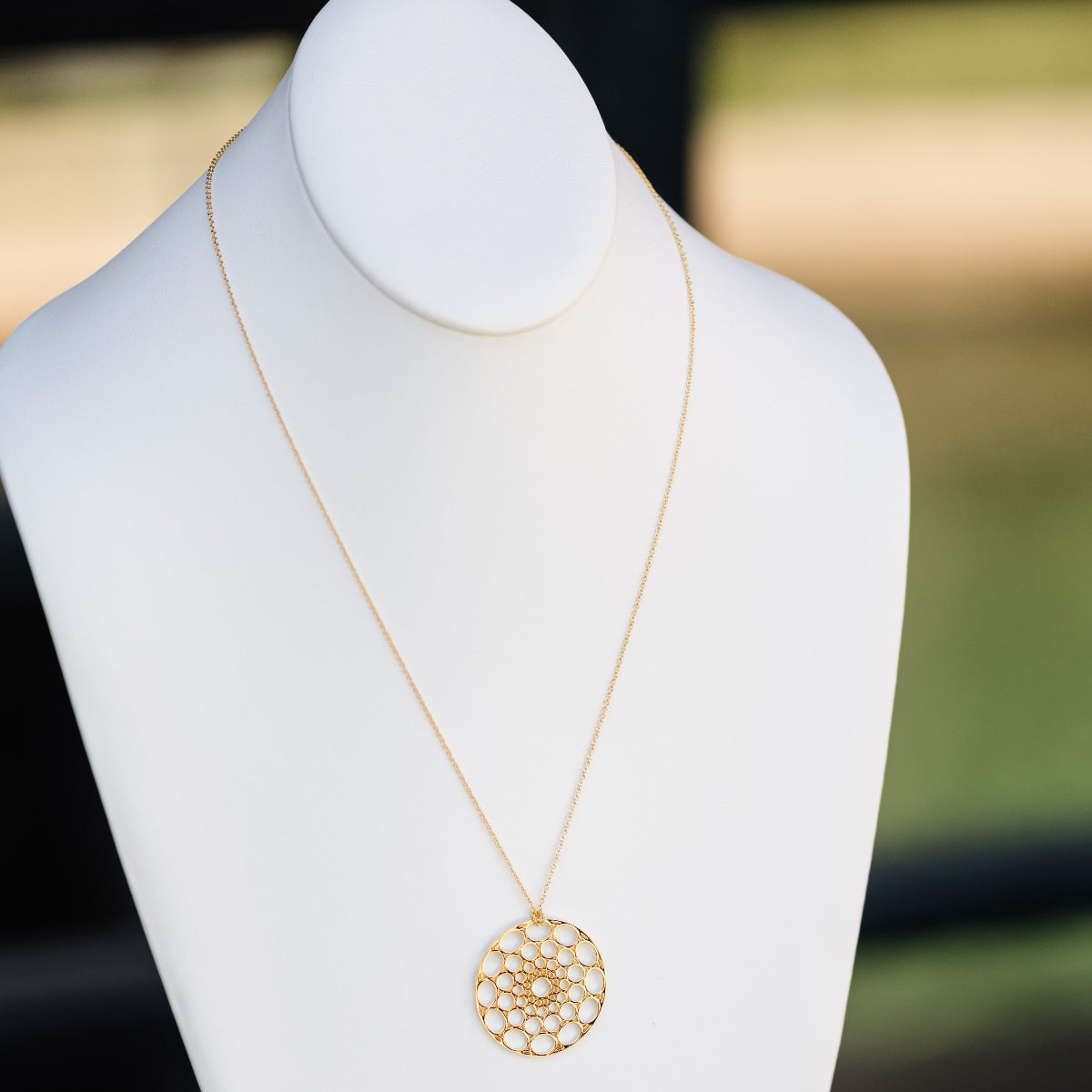 A Skylight Necklace in yellow gold on a white mannequin against a blurred background. 