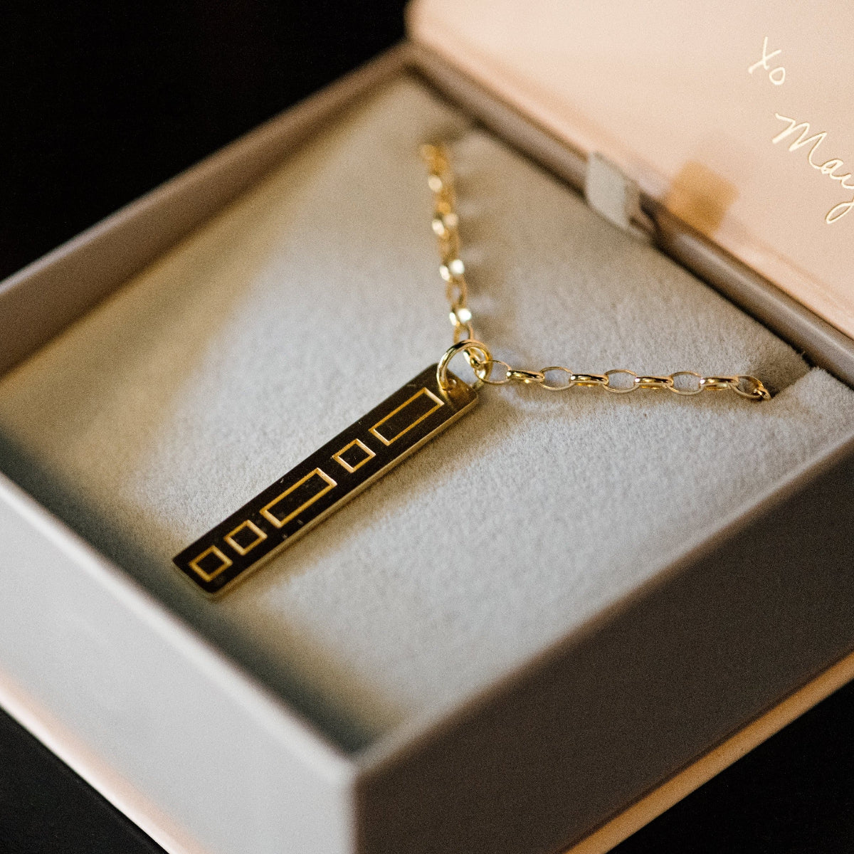 A Virtues Pendant - Rectangle in yellow gold in a Maya Brenner light grey and pink jewellery box against a black background. 