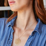 Close-up of a woman's neck wearing a Skylight Necklace in yellow gold with a blue denim shirt against a blurred background. 