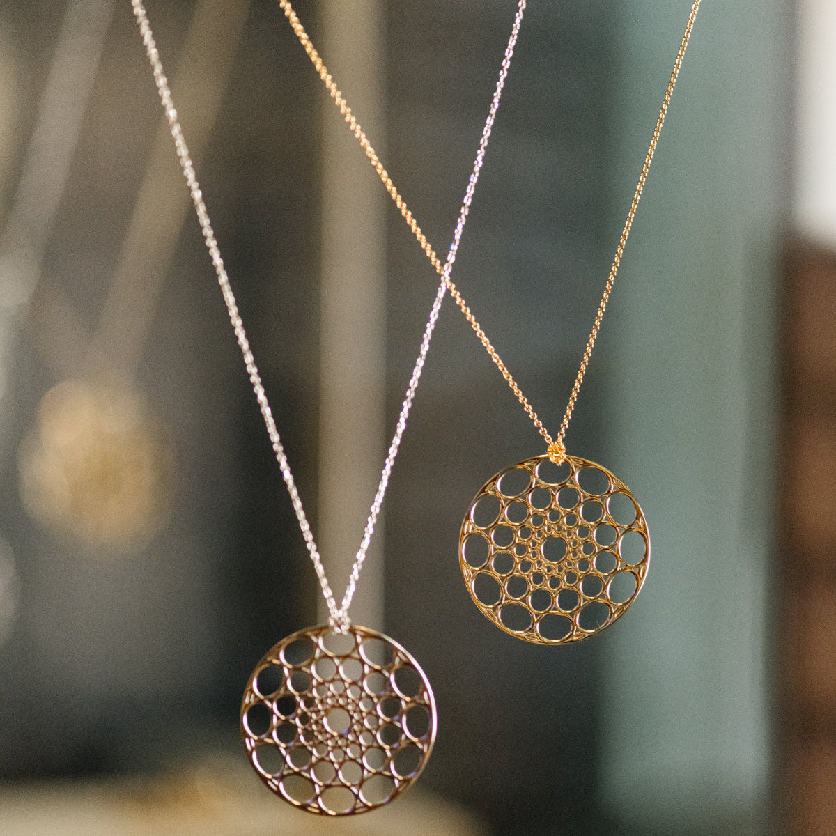 Two Skylight Necklaces in yellow gold against a blurred background. 