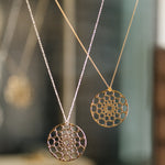 Two Skylight Necklaces in yellow gold against a blurred background. 