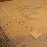 A Virtues Pendant - Square on top of a paper with sketches and writing. 