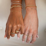 Two hands wearing several bracelets and rings in yellow and white gold: a Bold Link Bracelet, an Element Long Link Bracelet, two BFF Bracelets, a Down the Line Bracelet, a Love Set Match Bracelet, a Geo Stacking Ring, an Etched Paris Ring, a Link Ring and an Open Diamond Ring, against a neutral background.