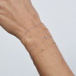 Gold bracelets with letter charms on a wrist against a light gray background