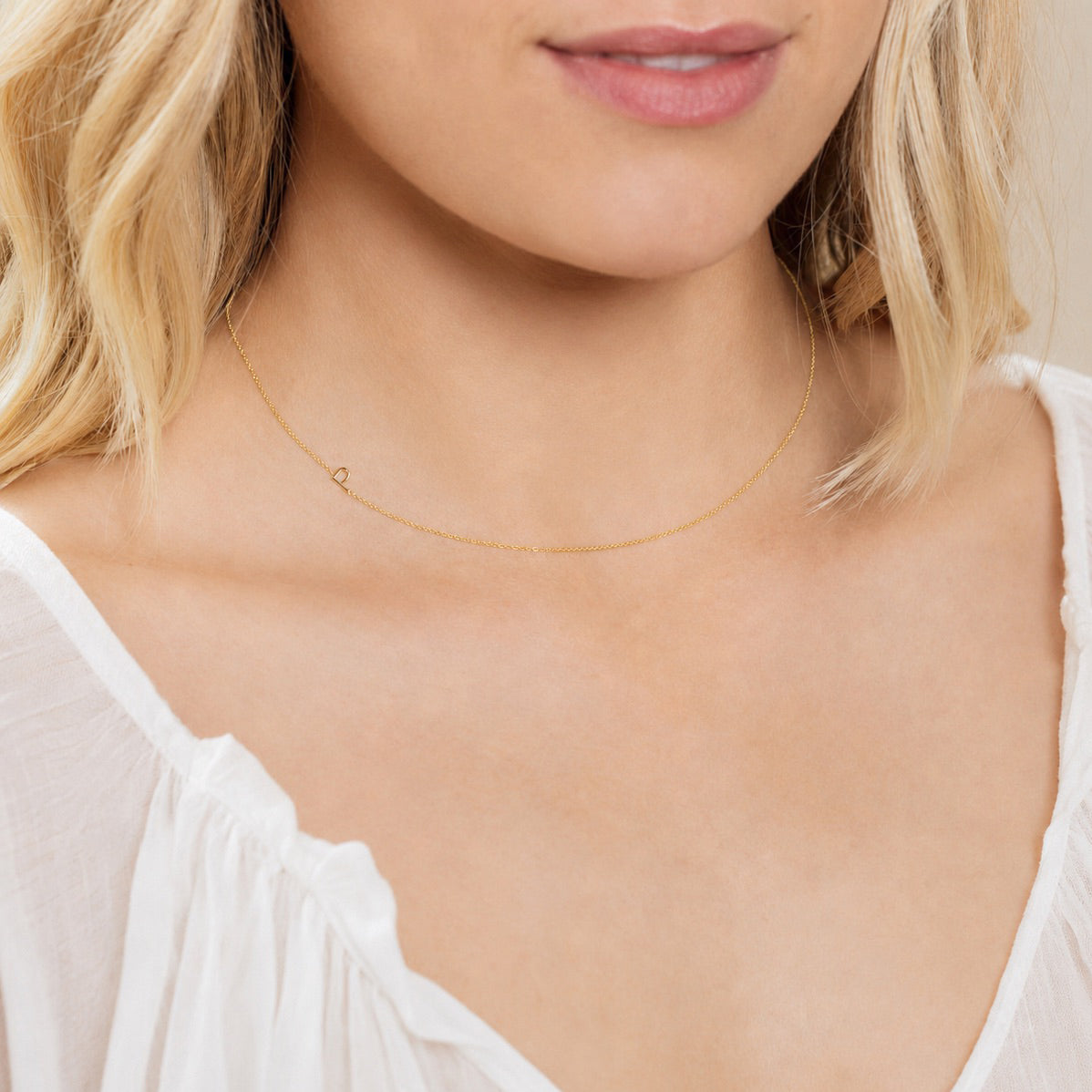 A close-up of a woman's neck wearing a yellow gold necklace with a letter P charm. 
