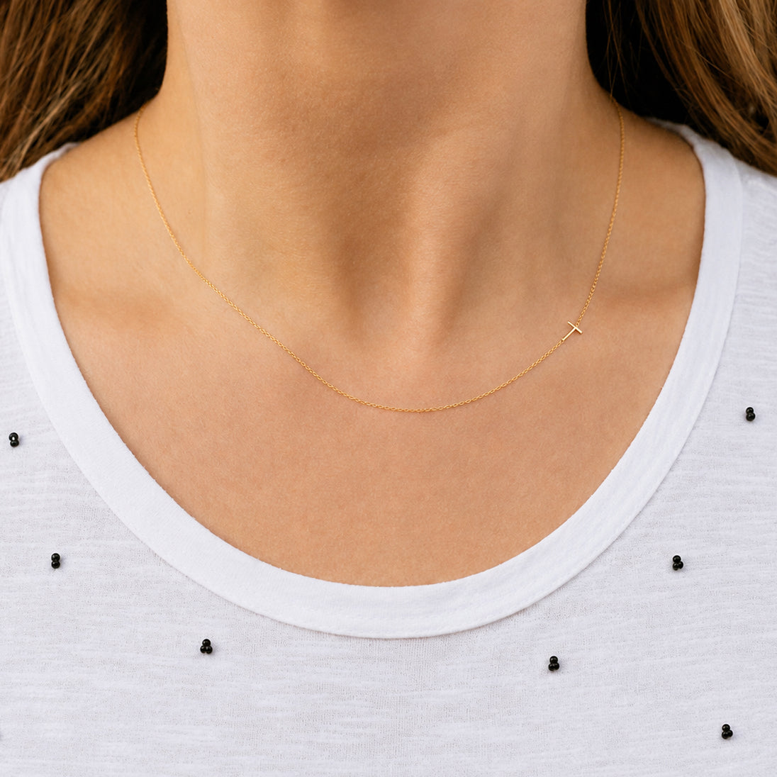 Gold Letter T necklace worn by a person on a white top with black embellishments.