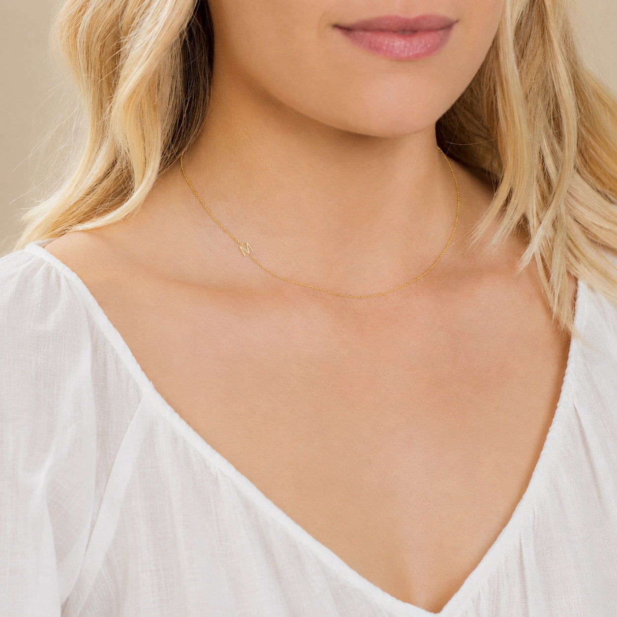 Close-up of a woman's neck wearing a yellow gold necklace with a letter M charm. 