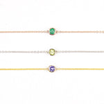 Three 14K Gold Asymmetrical Birthstone Necklaces - Emerald (May) in rose gold, Peridot (August) in white gold and Tanzanite (December) in yellow gold on a white background. 