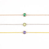 Three 14K Gold Asymmetrical Birthstone Necklaces - Emerald (May) in rose gold, Peridot (August) in white gold and Tanzanite (December) in yellow gold on a white background. 