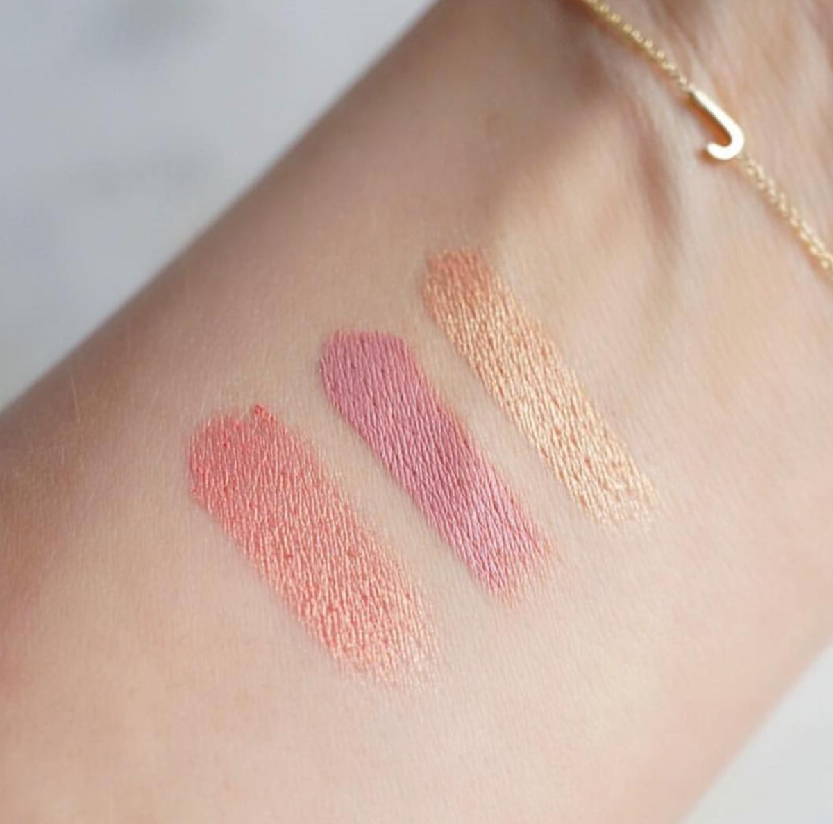 Three swatches of makeup colours on a person's arm with a Custom Gold Bracelet - 1 Letter with a letter J charm. 