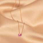 The Sweetheart Necklace - Pink Sapphire laid on top of peach silk fabric. 