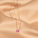 The Sweetheart Necklace - Pink Sapphire laid on top of peach silk fabric. 