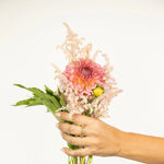 A hand wearing two The Daisy Bouquet Rings holding a bunch of flowers against a light grey background. 