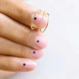 A hand holding a yellow gold Delicate Band, Delicate Beaded Band and Delicate Twist Band with pink nails against a white background. 