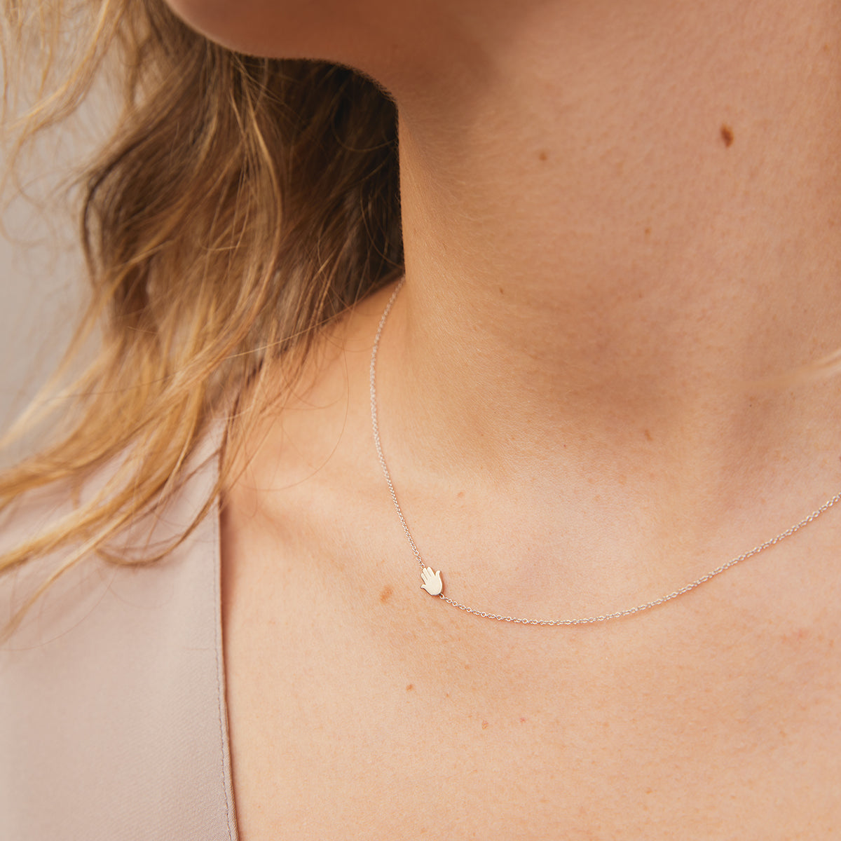 A close-up of a neck wearing a white gold 14k Gold Asymmetrical Charm Necklace - Hamsa with a cable chain. 