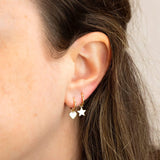 Close-up of Charmed I'm Sure Hoops in Heart and Star shown on a brunette woman's ear against a light grey background. 