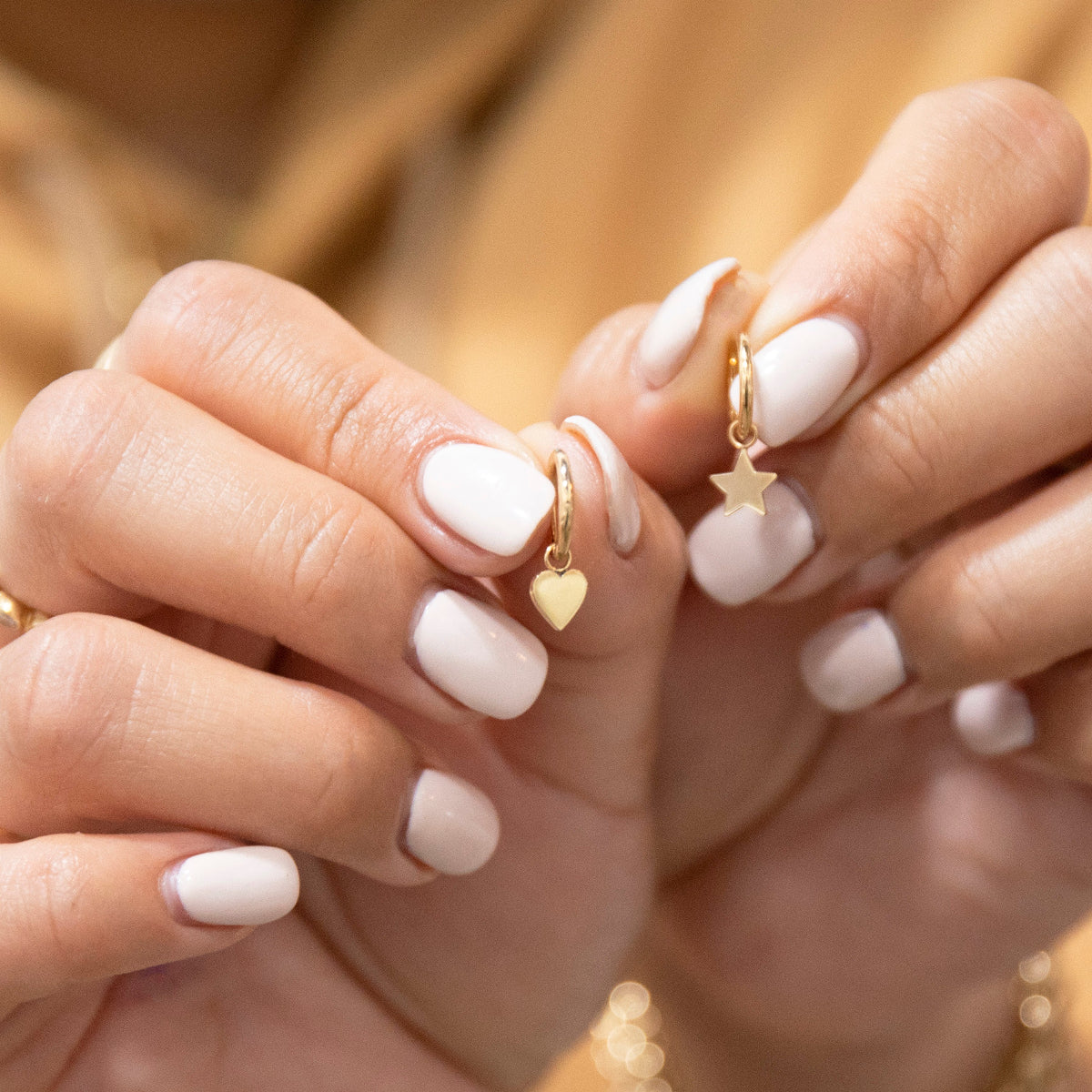 Charmed I'm Sure Hoops, one Star and the other Heart, being held by hands with light nails against a blurred background. 